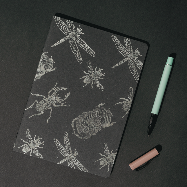 Libreta Econotas Alpen 15×21 cm color negro con ilustraciones de insectos en foil plateado y 32 hojas ecológicas cosidas en hilo.